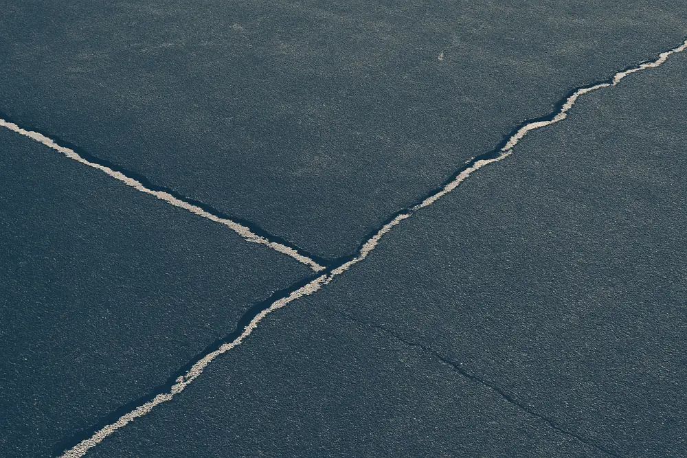 A close view of cracks running across a dark asphalt court surface — tennis court resurfacing, Adelaide. Illustrative example.