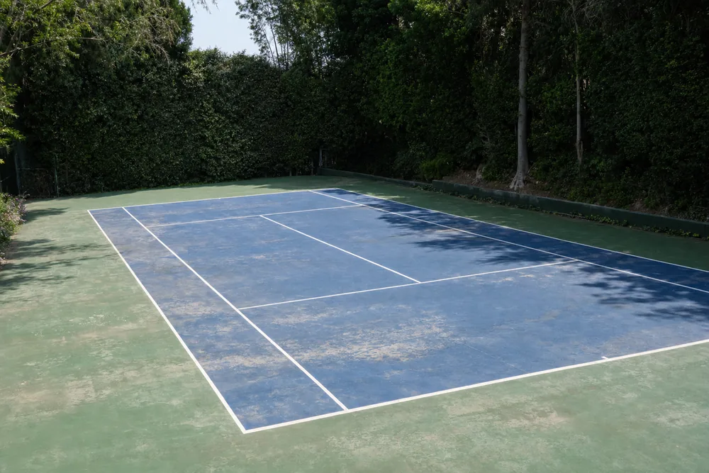 An empty acrylic hard court seen from a raised angle, faded blue and green — tennis court resurfacing, Adelaide. Illustrative example.